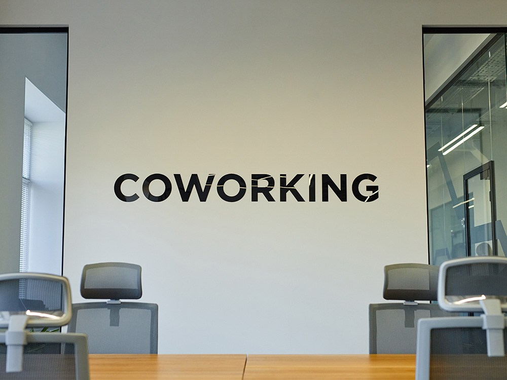 A modern coworking space with a wall featuring the word "COWORKING" in custom office wall decals and several ergonomic chairs and desks.