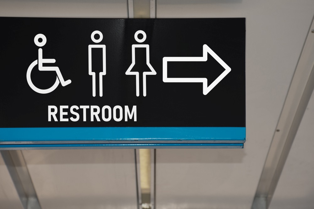 A restroom sign crafted by a signage company in Singapore, featuring icons for disabled, male, and female users along with an arrow pointing to the right.