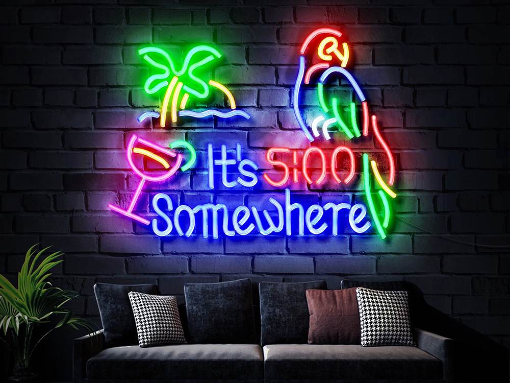 A backlit neon sign showing a parrot, a palm tree, and a drink with the text "It's 5 O'Clock Somewhere" hangs above a dark sofa against a brick wall.