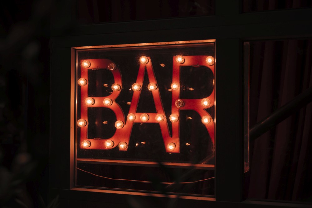 A window with the word "BAR" illuminated by backlit signage in a dark setting.